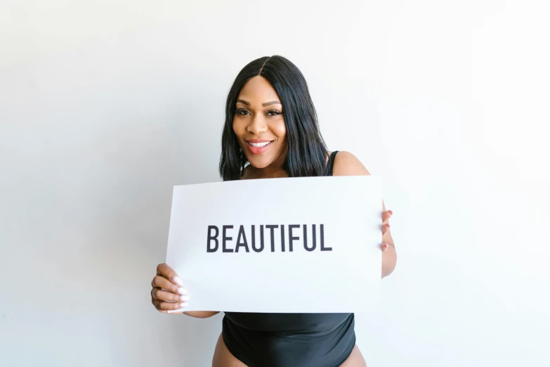 a woman holding a sign that says beautiful, an album cover, pexels contest winner, photoshoot for skincare brand, serena williams, with a white background, beautiful curves
