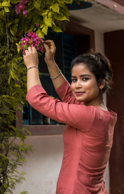 a woman standing in front of a building holding a bunch of flowers, inspired by T. K. Padmini, pexels contest winner, action pose, teenage girl, assamese, in garden