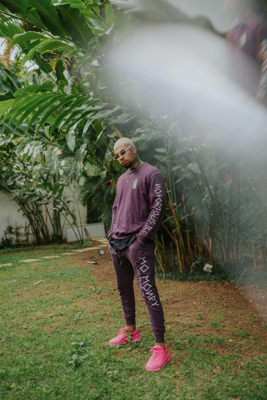 a man standing on top of a lush green field, an album cover, by Cosmo Alexander, pexels contest winner, graffiti, wearing a purple sweatsuit, joseph moncada, non-binary, standing outside a house