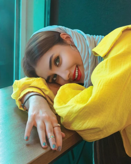 a woman laying on top of a table next to a window, an album cover, inspired by Maryam Hashemi, trending on pexels, wearing a yellow hoodie, beautiful iranian woman, gif, smirking