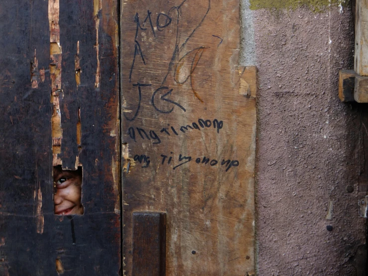 a close up of a door with graffiti on it, an album cover, by Matteo Pérez, tortured face made of wood, slum, tiny person watching, signatures