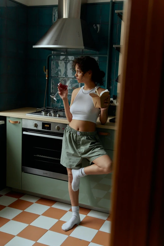 a woman standing in a kitchen next to a stove, inspired by Elsa Bleda, pexels contest winner, renaissance, playful pose of a dancer, bra and shorts streetwear, wine, kiko mizuhara