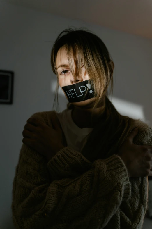 a woman with a tape around her mouth, by Adam Marczyński, trending on pexels, antipodeans, black bandage on arms, woman his holding a sign, girl with brown hair, wearing turtleneck