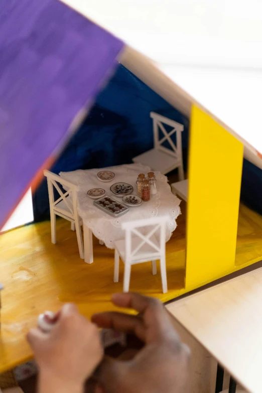 a close up of a person playing with a doll house, inspired by Hendrick Avercamp, visual art, in a colorful tent, dining table, yellow and purple color scheme, experimental studio light