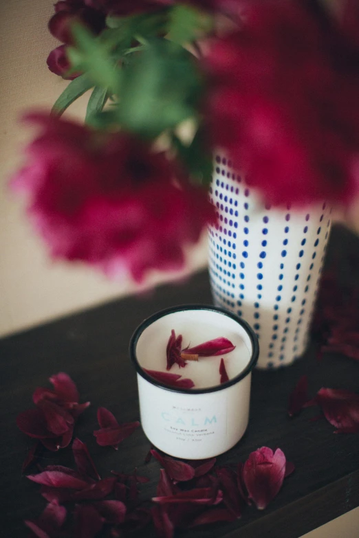 a candle sitting on top of a table next to a vase of flowers, by Lucia Peka, unsplash, rose petals, hero shot, maroon and blue accents, black peonies