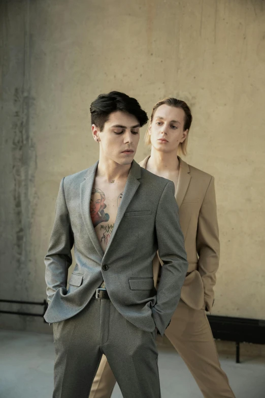 a woman standing next to a man in a suit, an album cover, by Winona Nelson, unsplash, bauhaus, portrait androgynous girl, beautiful male twins portrait, wearing a worn out brown suit, tattooed