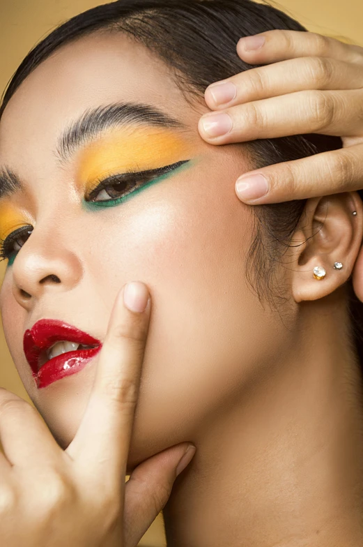 a woman with bright makeup holding her hand to her face, inspired by Ina Wong, trending on pexels, yellow and green, beauty campaign, asian female, high angle close up shot