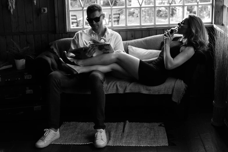 a man and a woman sitting on a couch, a black and white photo, by Emma Andijewska, with sunglass, reading a book, stoya, sleek legs