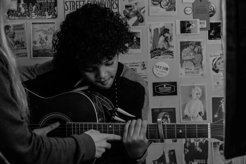 a black and white photo of a person playing a guitar, an album cover, pexels contest winner, curly afro, real guitars hanging on the wall, teenage boy, compassionate