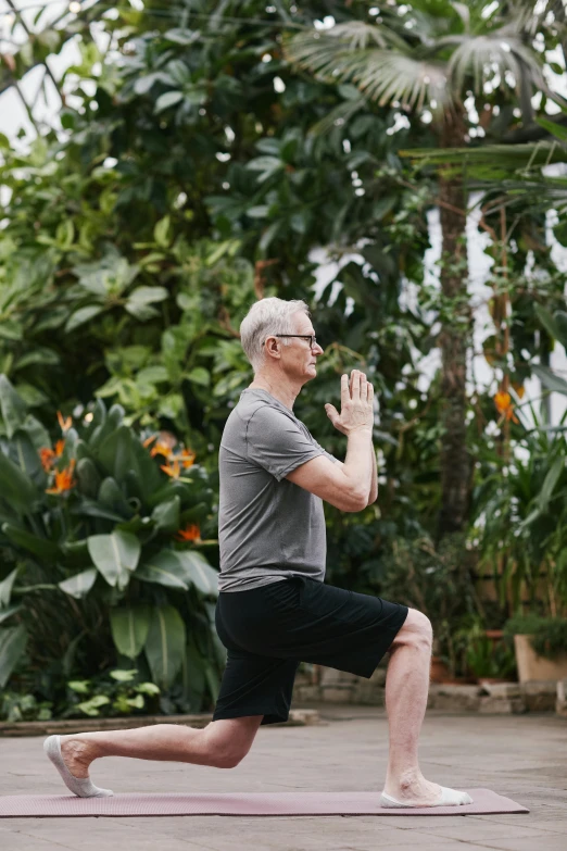 a man doing a yoga pose on a yoga mat, inspired by Graham Forsythe, unsplash, standing in a botanical garden, man with glasses, 70 years old, david spade