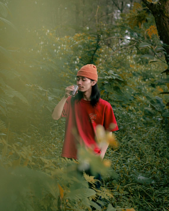 a man standing in the woods talking on a cell phone, inspired by Elsa Bleda, unsplash contest winner, color field, wearing a marijuana t - shirt, wearing red attire, queer woman, mingchen shen