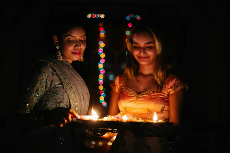 two women holding lit candles in a dark room, a portrait, pexels, hurufiyya, hindu ornaments, happy birthday, square, multicoloured