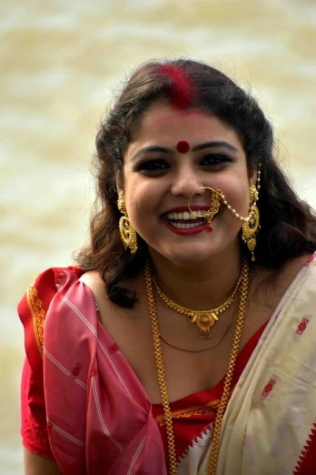 a woman in a sari smiling for the camera, by Sudip Roy, face piercings, gold and red accents, slide show, assamese