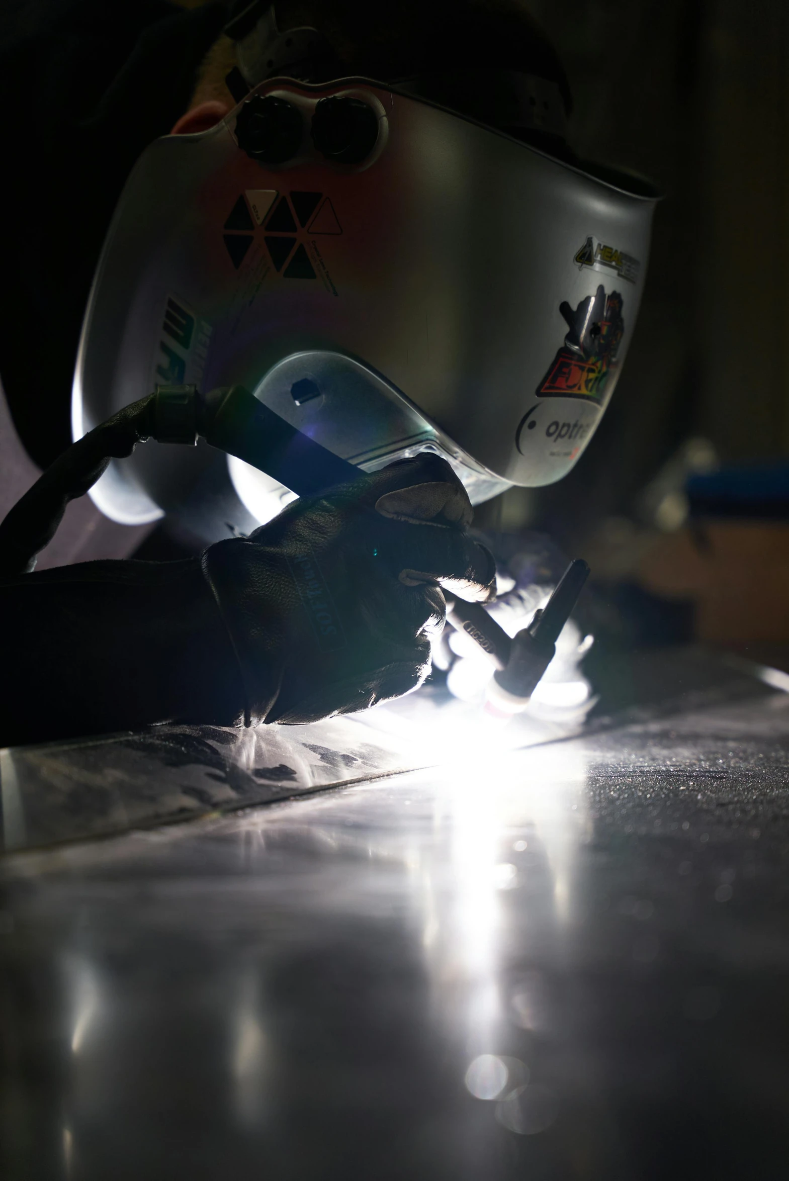 a person welding a piece of metal on a table, glow around helmet, aluminium, lachlan bailey, close - up photograph