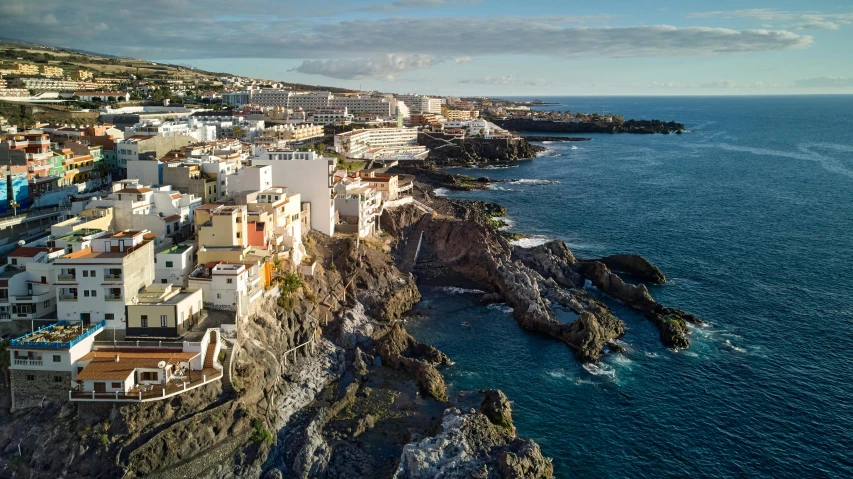 a group of buildings sitting on top of a cliff next to the ocean, a photo, spanish, white lava, travel guide, thumbnail