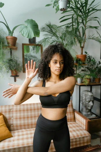 a woman standing in a living room next to a couch, trending on pexels, renaissance, karate pose, wearing a cropped top, mixed-race woman, hands reaching for her