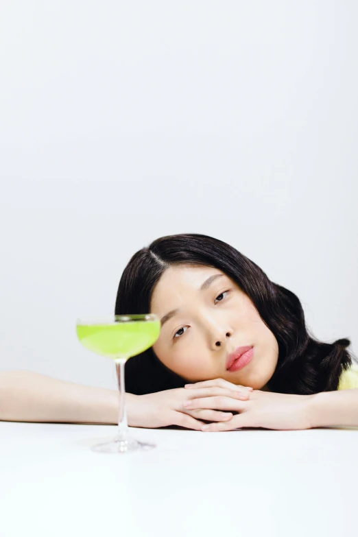 a woman sitting at a table with a glass of wine, an album cover, inspired by Ren Hang, unsplash, lime green, ethnicity : japanese, drinking a martini, disappointed