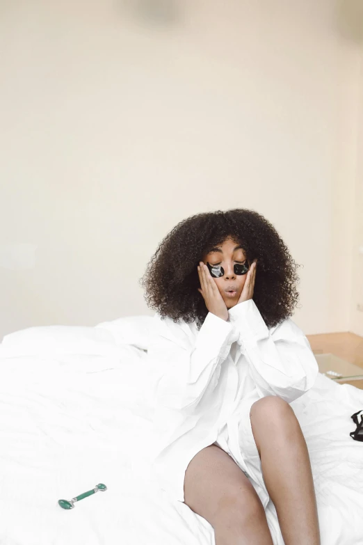 a woman sitting on a bed talking on a cell phone, an album cover, by Dulah Marie Evans, trending on pexels, long afro hair, sleek robes, big eyes, all white