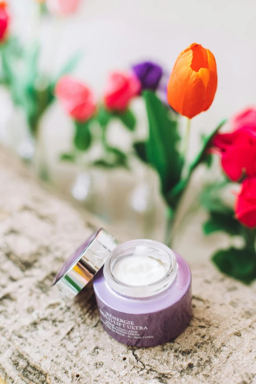 a jar of cream sitting on top of a table next to flowers, trending on pexels, soft purple glow, textured base ; product photos, skincare, multicoloured