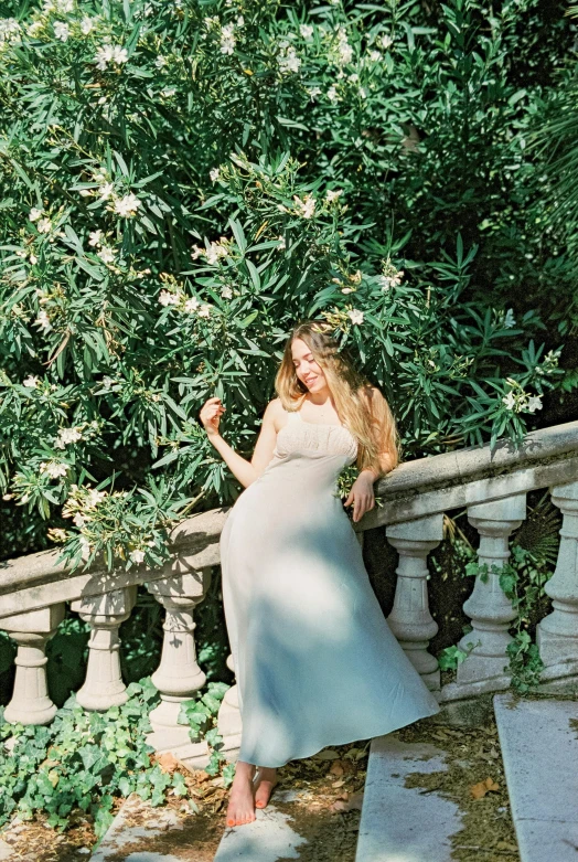 a woman in a white dress leaning on a railing, inspired by Oleg Oprisco, unsplash, renaissance, archways made of lush greenery, elegant smiling pose, light green dress, sydney sweeney