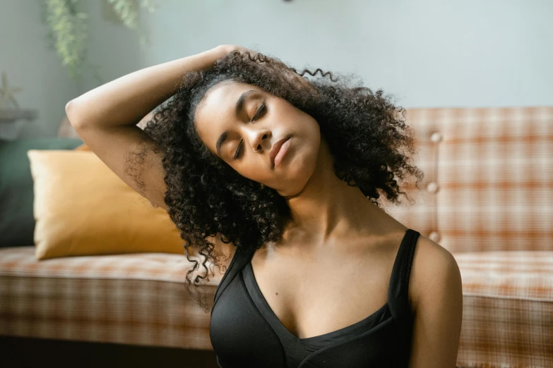 a woman sitting on a couch with her eyes closed, trending on pexels, renaissance, black bra, with curls, morning time, black ponytail