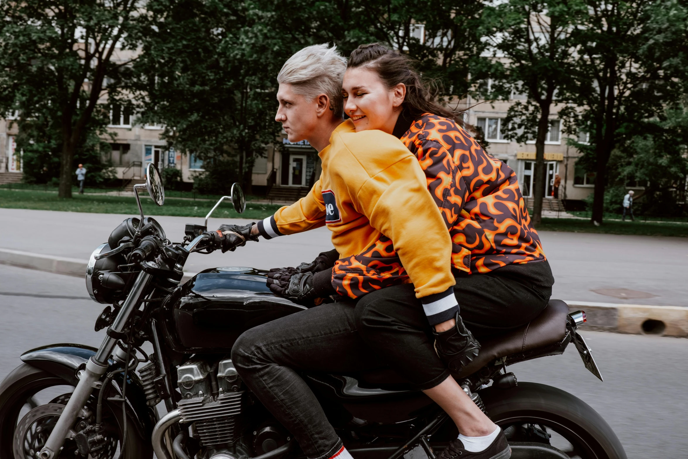 a man and woman riding on the back of a motorcycle, by Emma Andijewska, pexels contest winner, happening, patterned clothing, long orange sweatshirt, non-binary, russian girlfriend