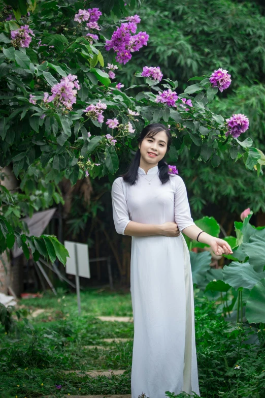 a woman in a white dress standing in a garden, a picture, inspired by Cui Bai, pexels contest winner, ao dai, purple, wearing a hoodie and flowers, at home