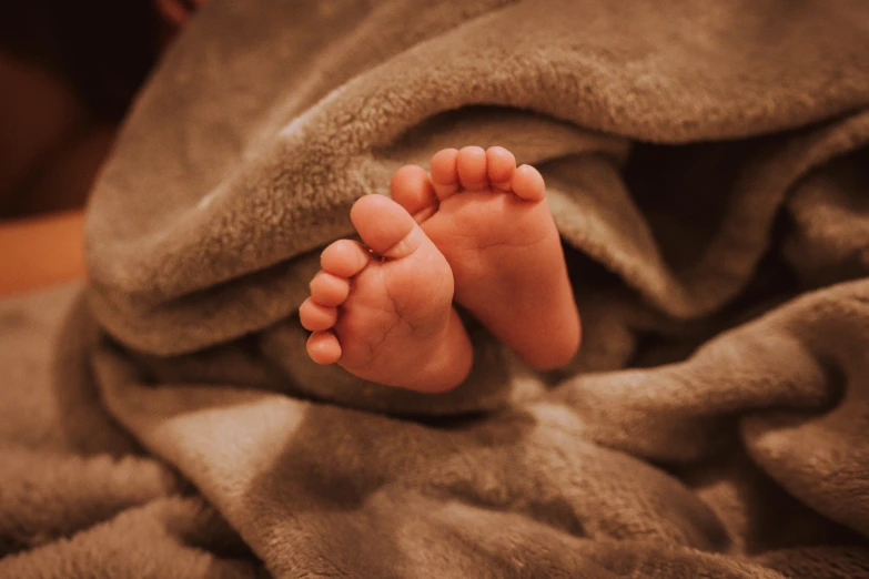 a close up of a person's feet under a blanket, pexels, human babies, wearing brown robes, hatched ear, late evening