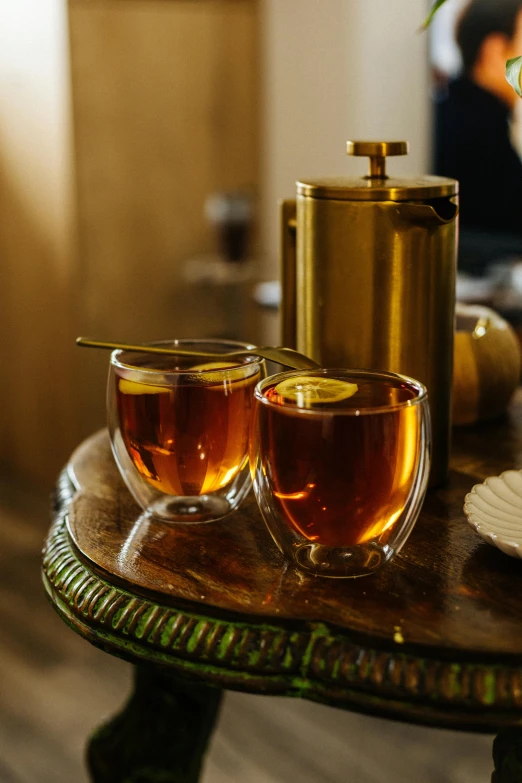 two cups of tea on a table in front of a tv, a still life, inspired by Kanō Shōsenin, unsplash, renaissance, glass and gold pipes, ambient amber light, jaquet droz, full body in shot