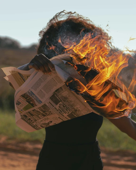 a woman holding a newspaper in front of a fire, an album cover, pexels contest winner, on a hot australian day, burning overgrowth, photo of a black woman, ignant