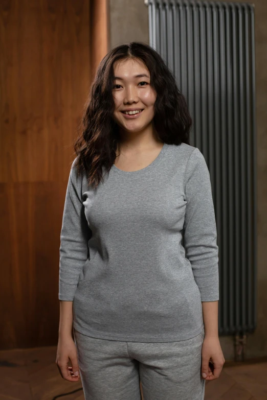 a woman standing in front of a radiator, inspired by Kim Tschang Yeul, gray shirt, academic clothing, dark grey backdrop studio, vp of marketing