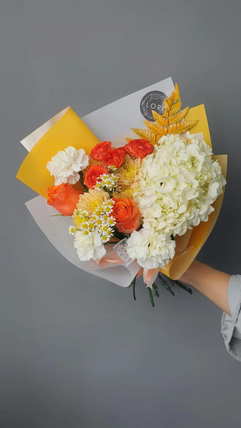 a person holding a bouquet of white and orange flowers, on grey background, yellow and orange color scheme, say ahh, designed for cozy aesthetics!