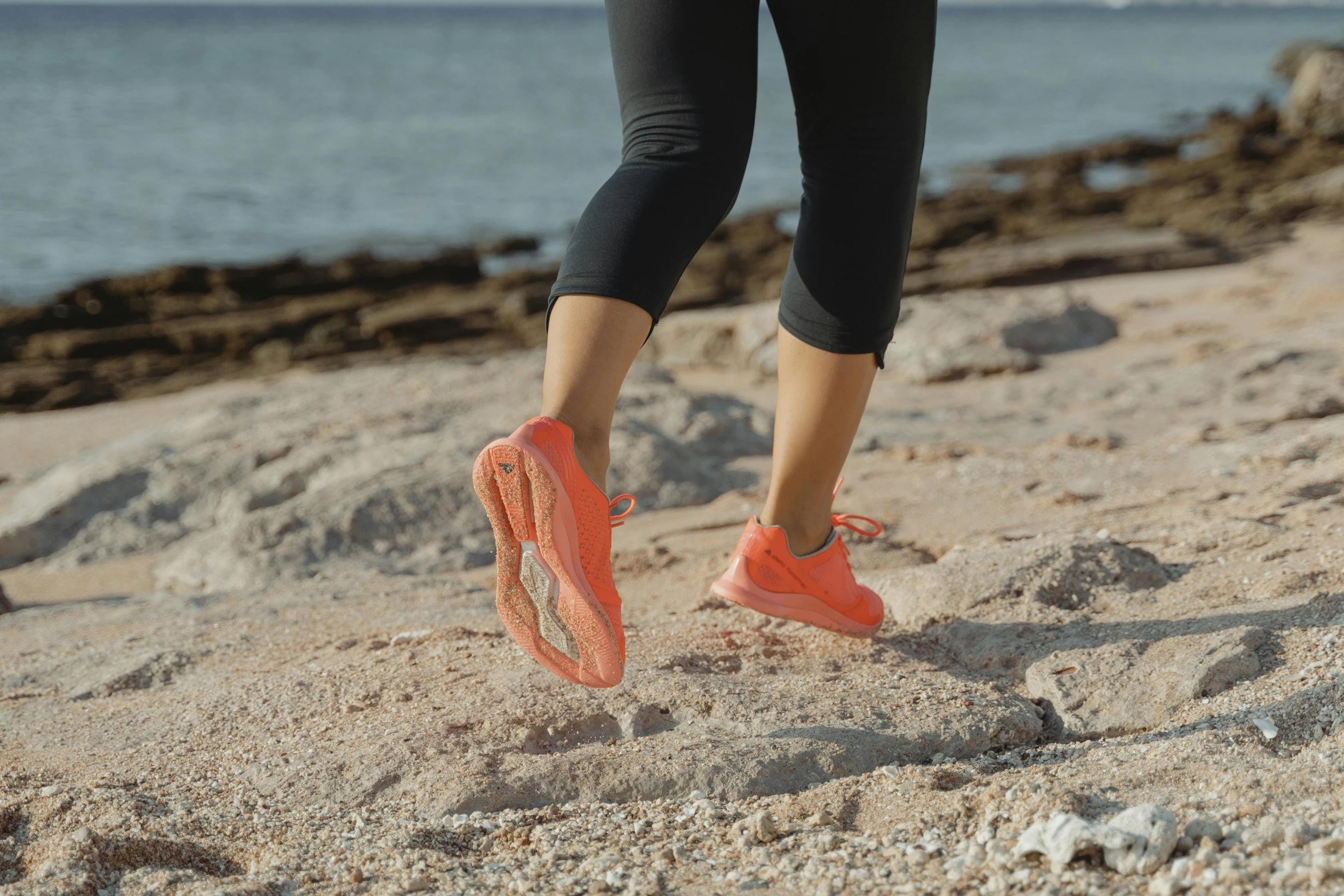 a woman walking on top of a sandy beach, running shoes, in shades of peach, puma, action shot