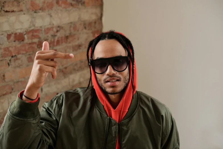 a man standing in front of a brick wall, an album cover, trending on pexels, wearing glack glasses, raffael, with pointing finger, thumbnail