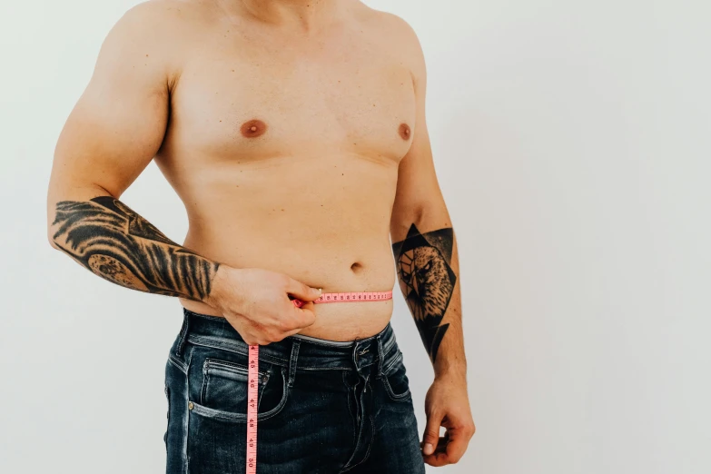 a man measuring his waist with a tape, a tattoo, trending on pexels, plain background, background image, shirtless biden with tatoos, wearing casual clothes