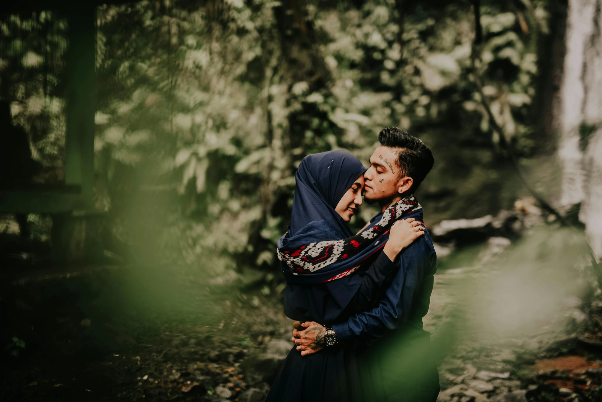 a couple standing next to each other in a forest, a picture, pexels contest winner, sumatraism, hijab, thumbnail, embracing, man