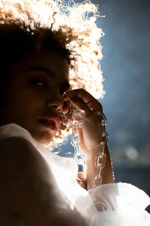 a woman in a white dress holding a cell phone to her ear, an album cover, inspired by Elsa Bleda, trending on pexels, visual art, thick glowing chains, imaan hammam, glowing with silver light, close - up photograph