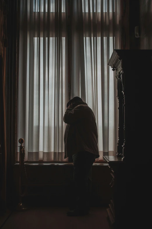 a person sitting on a bed in front of a window, pexels contest winner, romanticism, two men hugging, she's sad, standing in corner of room, hood and shadows covering face