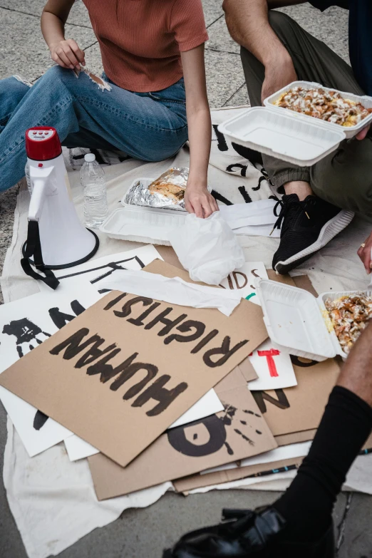 a group of people sitting on the ground eating pizza, trending on unsplash, graffiti, protest, cardboards ; mess, hannah yata, protest movement