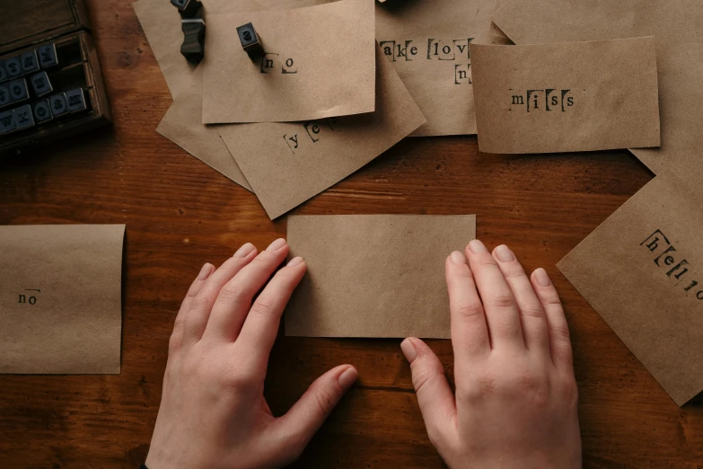 a person holding a piece of paper on top of a wooden table, by Emma Andijewska, pexels contest winner, letterism, brown colors, many pieces, thumbnail, holiday