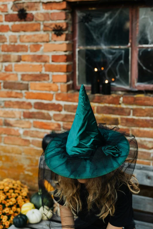 a woman sitting on a bench wearing a witches hat, pexels, flowing teal-colored silk, ( ( dark green, square, kids