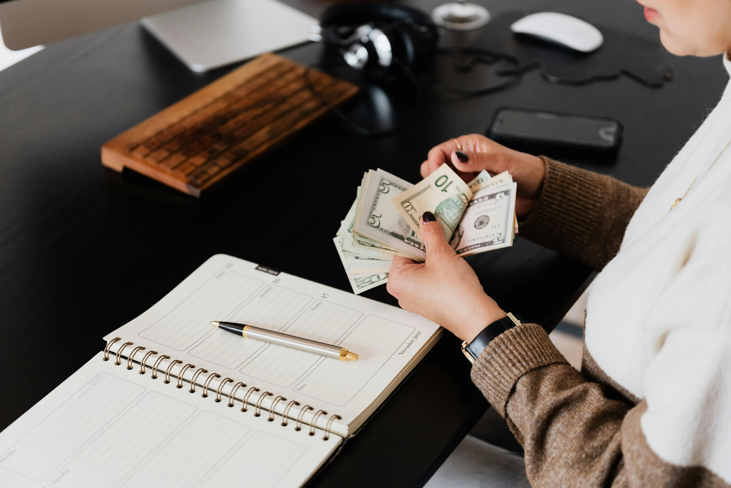 a woman sitting at a desk holding a stack of money, by Julia Pishtar, pexels contest winner, hurufiyya, 🦩🪐🐞👩🏻🦳, pen and paper, carson ellis, a wooden