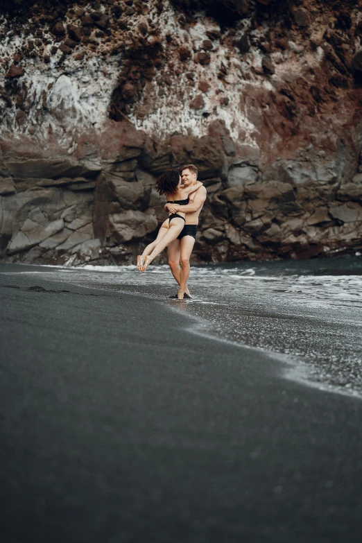 a woman standing on top of a beach next to the ocean, couple dancing, black sand, mateo dineen, in a sea