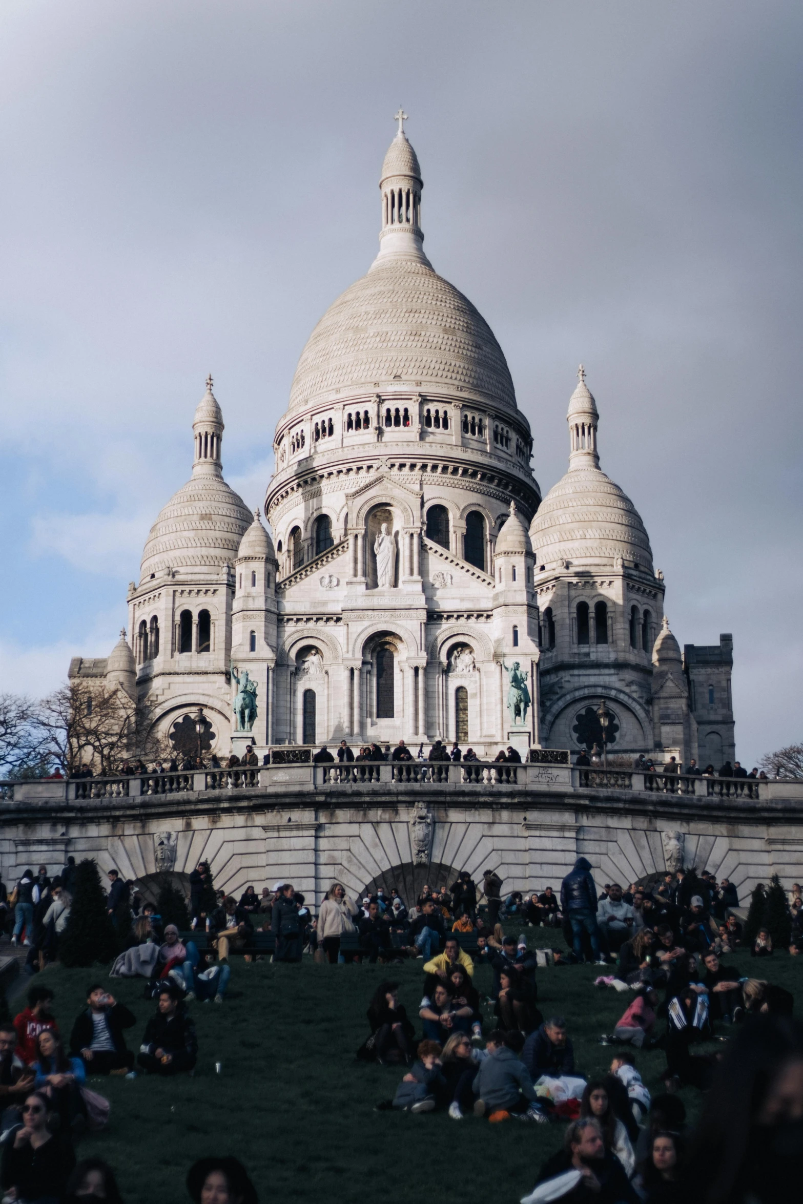 a group of people sitting on the grass in front of a building, trending on unsplash, paris school, dome, low quality photo, elevation view, cathedral!!!!!