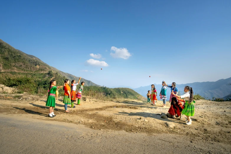 a group of people standing on top of a dirt field, ao dai, kids playing, hills, vibrant red and green colours