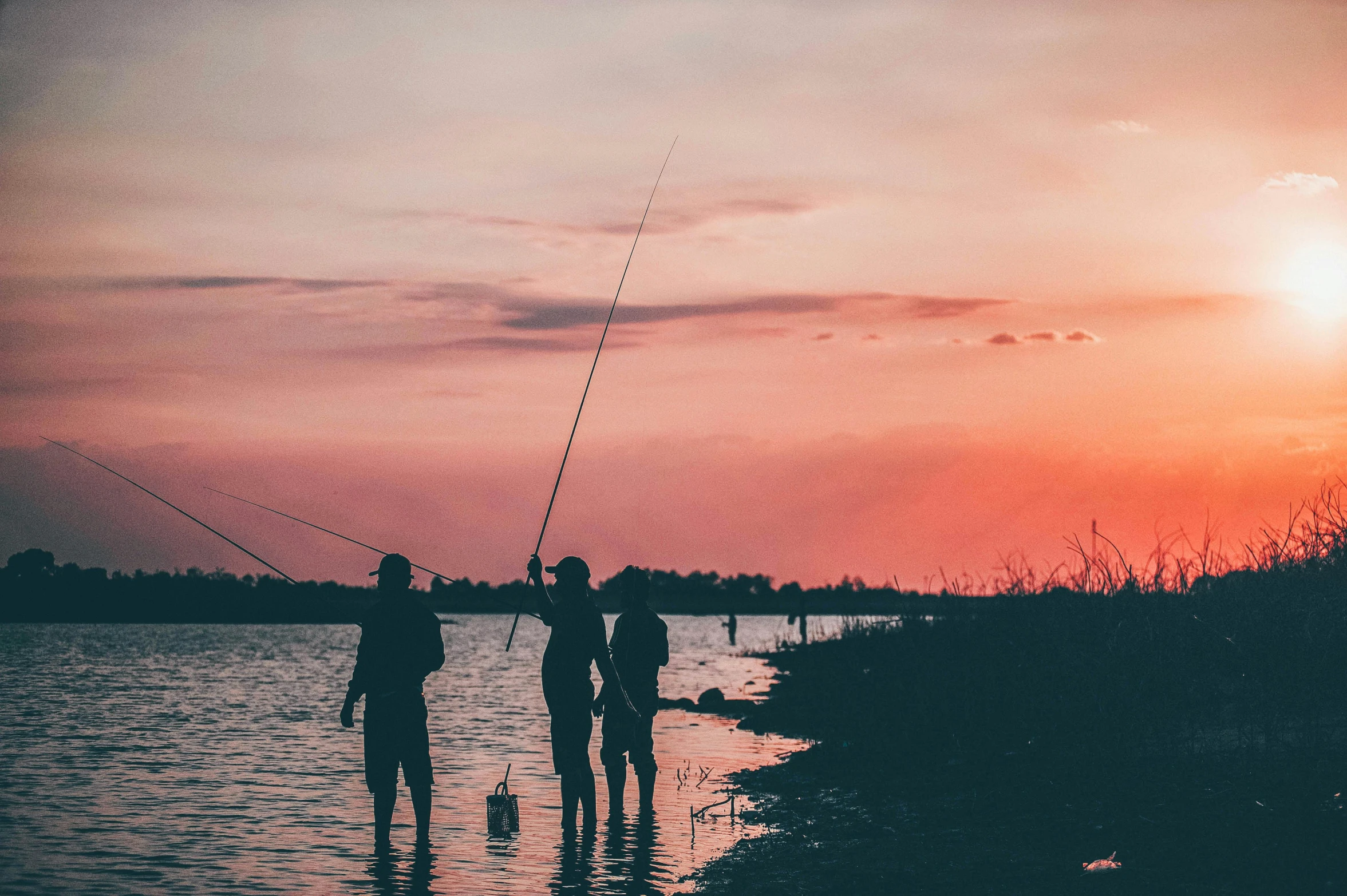 a couple of people that are standing in the water, by Jesper Knudsen, pexels contest winner, fishing pole, pink sunset, vintage photo, banner