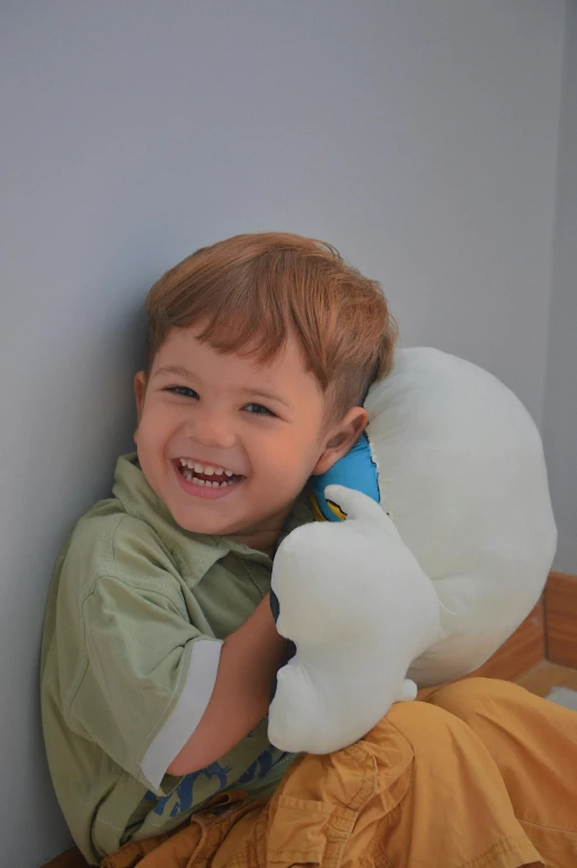 a young boy sitting on a bed holding a stuffed animal, inspired by Arshile Gorky, trending on reddit, head bent back in laughter, holding a white duck, softplay, on a gray background