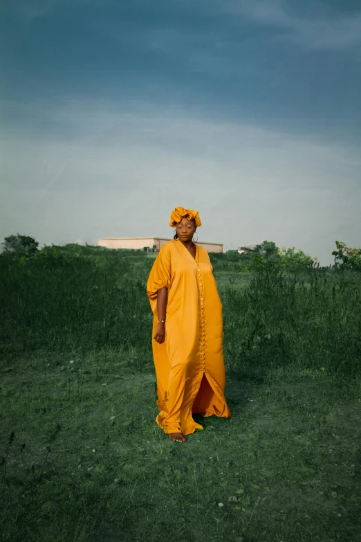 a man in a yellow outfit standing in a field, an album cover, by Chinwe Chukwuogo-Roy, pexels contest winner, somali woman, wearing a robe, annie leibowitz, analog photo