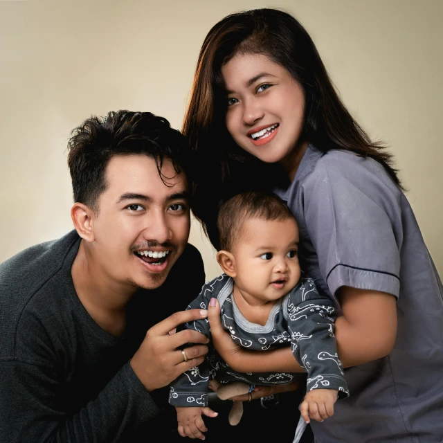 a man and woman pose for a picture with a baby, a picture, by Basuki Abdullah, pixabay contest winner, realism, plain background, 15081959 21121991 01012000 4k, dentist, handsome