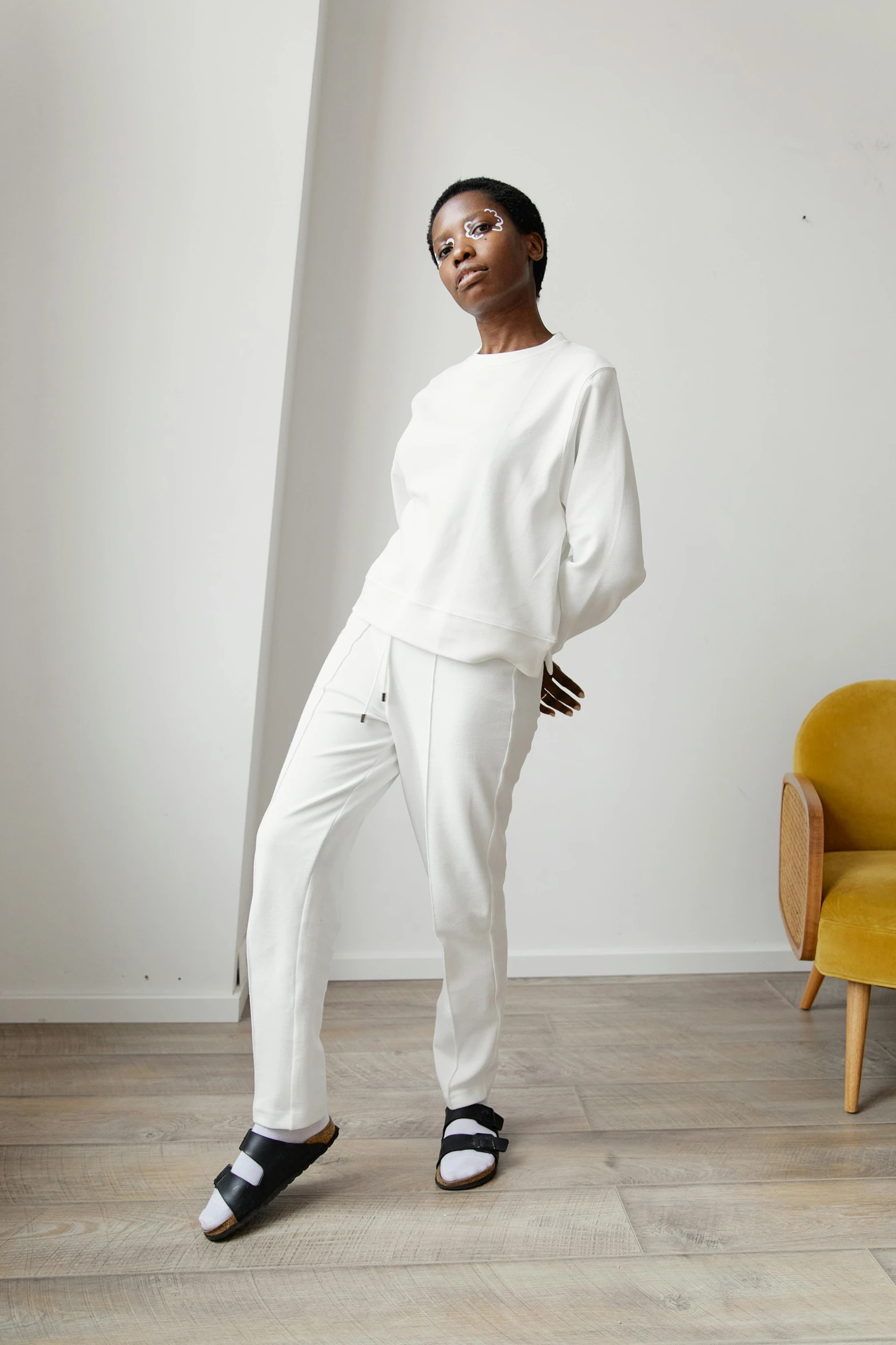 a woman standing in front of a yellow chair, wearing white pajamas, wearing sweatshirt, triple white colorway, curated collections